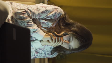 video vertical de una mujer joven viendo una película de terror en una computadora portátil por la noche.