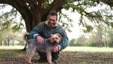 joyful moments in nature: a heartwarming bond between a man and his dog under a sprawling tree in a serene park setting