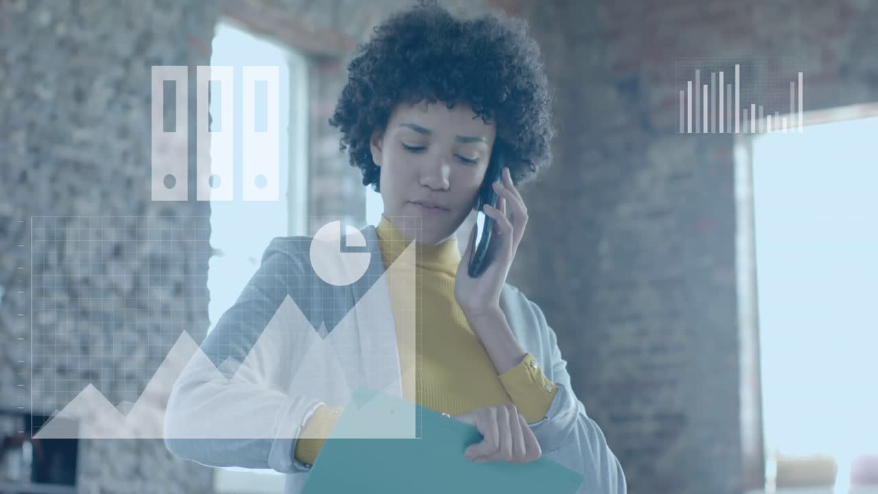 Animation of business icons over biracial businesswoman talking on smartphone in office