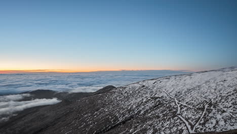 Snow-covered-landscape-at-dusk-with-a-clear-sky-transitioning-from-blue-to-orange-hues,-timelapse