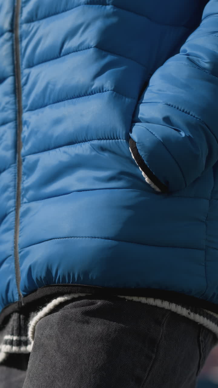 primer plano de un individuo con chaqueta azul sosteniendo una bolsa de compras, centrado en la mano y el bolsillo paseando, detalle contra un fondo al aire libre borroso