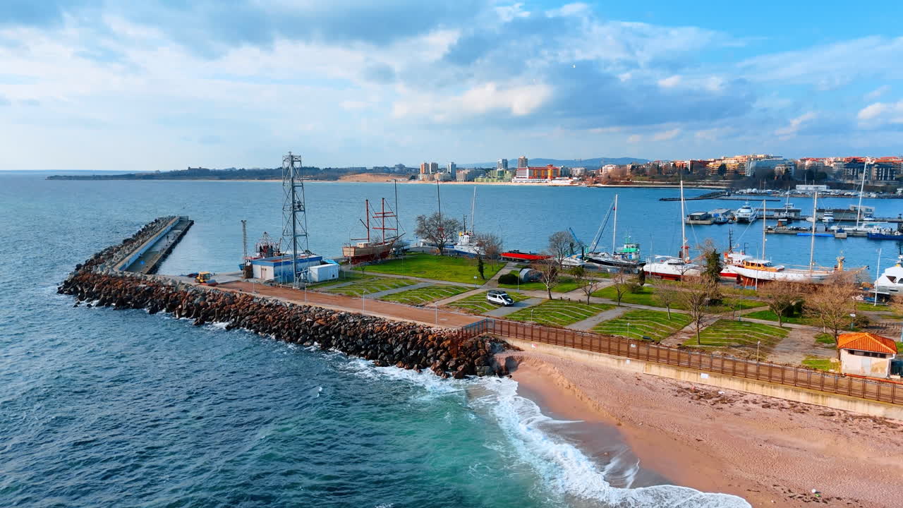 Nadmorski port i plaża widziane z góry. Ujęcie z wysoka przedstawiające molo, piaszczysty brzeg i łodzie zacumowane w marinie.