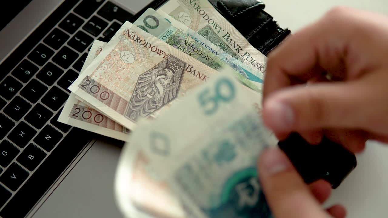 пересчитать деньги и положить их в черный кошелек, лежащий на ноутбуке, национальная валюта польши, денежная купюра польского злотого