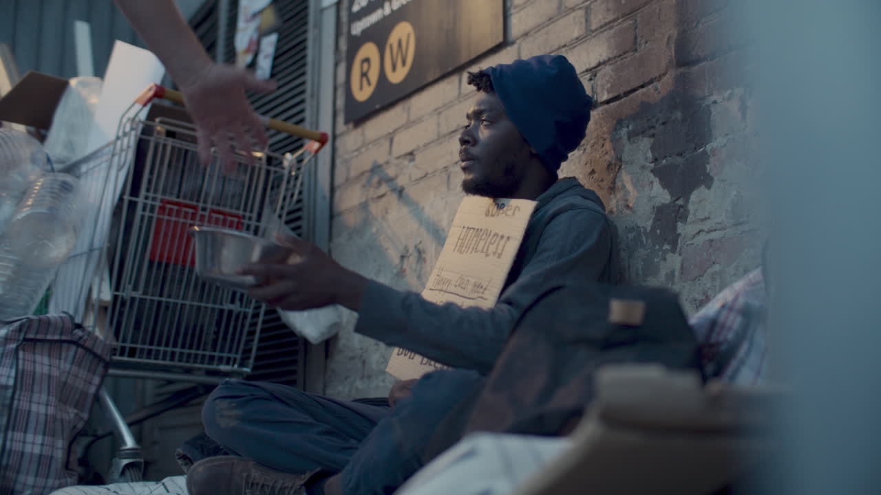 Homeless Beggar Sitting on Sidewalk, Receiving Donation from Passerby