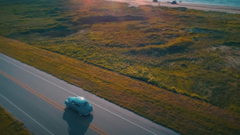 Aéreo-Coche-Clásico-Llamaradas-De-Sol-Hora-Dorada-Romántico-Paseo-Por-La-Playa-Puesta-De-Sol-Disparo-De-Drone-1940-Plymouth-4k