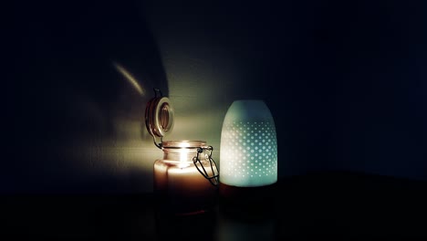 lit open flame candle in a glass jar beside a air humidifier that is changing colors while emitting a light stream of mist