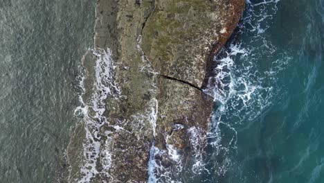 birdseye view top down aerial of waves crashing over protruding large rocks in ocean