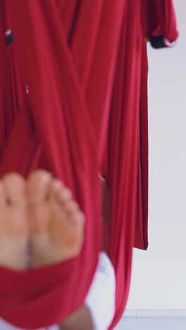 relaxed ladies practice modern aerial yoga pose lying in long red hammocks and improving mental health close view