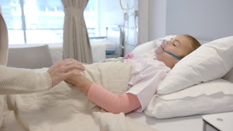 seção média de uma mãe caucasiana segurando a mão da filha paciente em uma cama de hospital, em câmera lenta