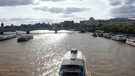 Forwards-tracking-of-passenger-ship-floating-on-shinny-surface-of-River-Thames.-Heading-towards-Waterloo-Bridge,-view-against-bright-sunshine.-London,-UK