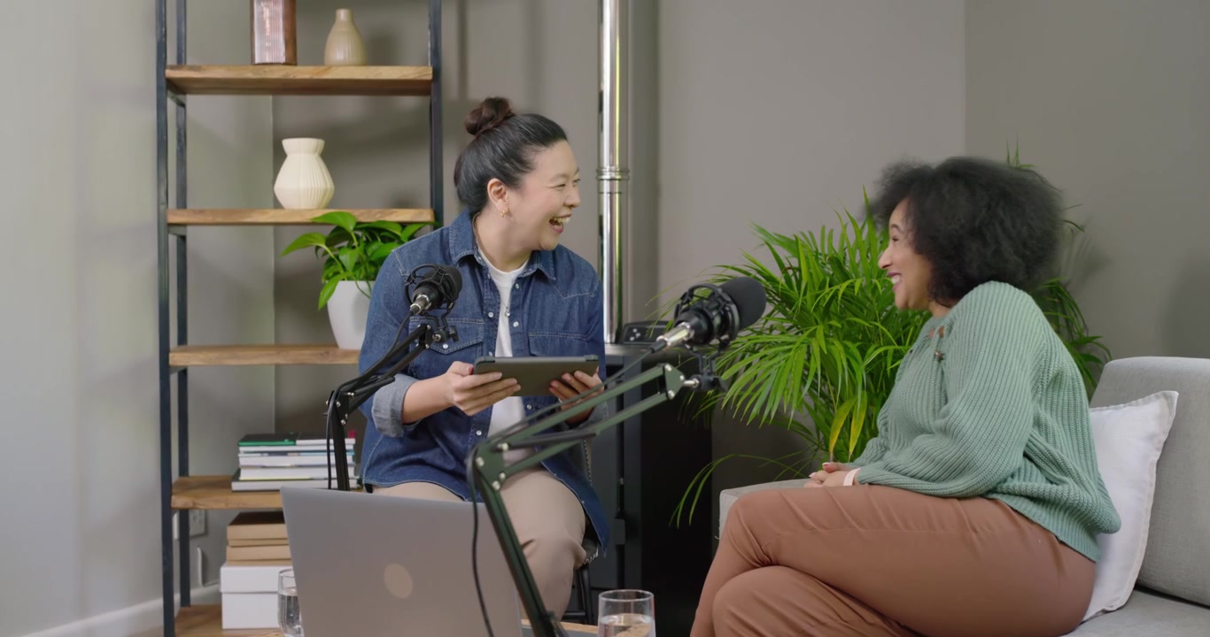 Aziatische presentator leest tablet, Afro-Amerikaanse gast lacht en gebaart met microfoons tijdens studio-interview