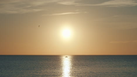 lonely boat sits at sea during sunset in sun's reflection, long shot