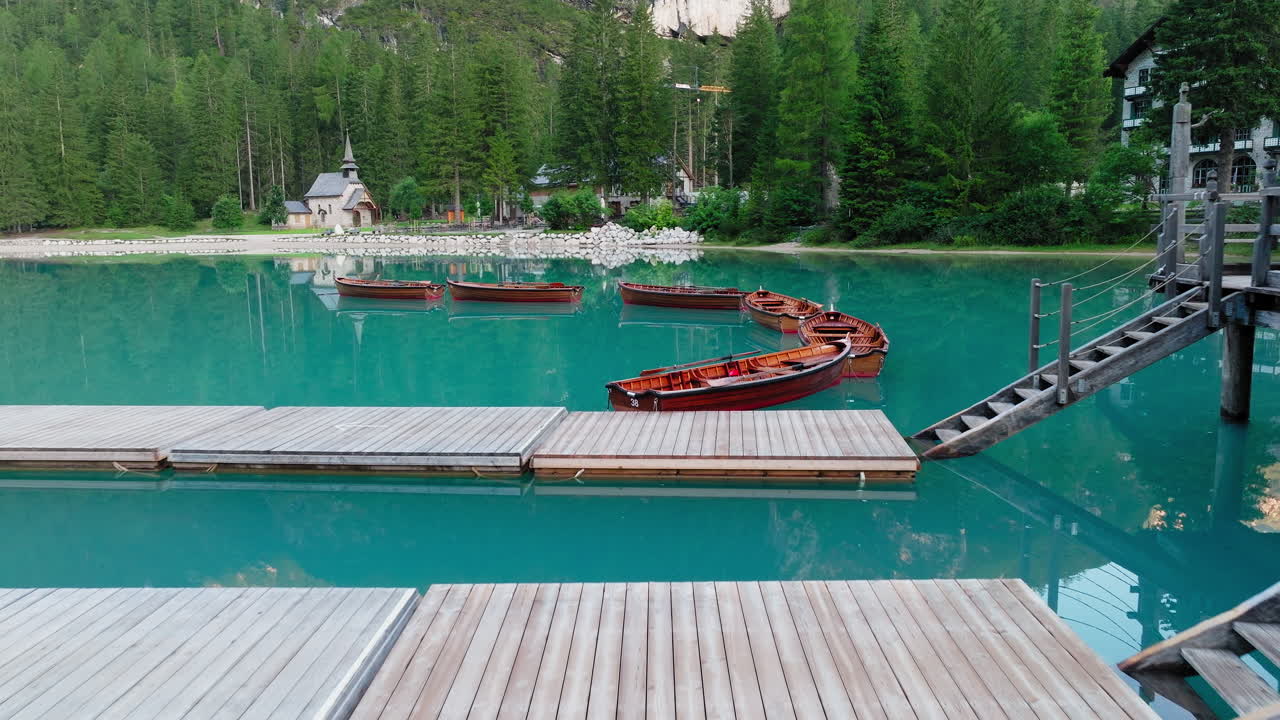 Lago di Braies or Lake Braies crystal blue lake with wooden rowing boats in Italian Dolomites, Lago di Braies chapel and coniferous and broadleaf trees in background, Closeup view