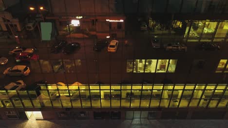 4k outside view of business district building , mall with wall mirror windows at evening or night .  reflection of city , people , cars in mirrored walls . drone camera moving . people working inside