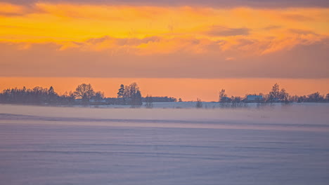 Picturesque-shot-of-sunrise-time-lapse-over-wooden-house-surrounded-by-trees-covered-in-snow-and-icy-winds-blowing