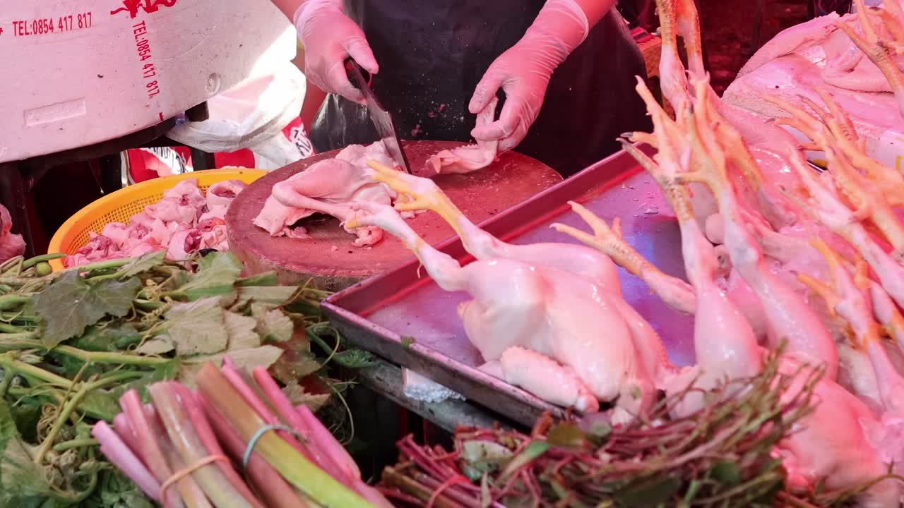A vendor skillfully handles poultry and fresh greens at a vibrant market stall.
