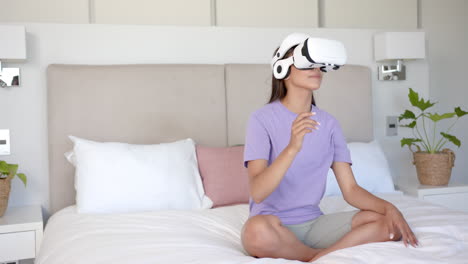 using vr headset, woman sitting cross-legged on bed in modern bedroom, copy space