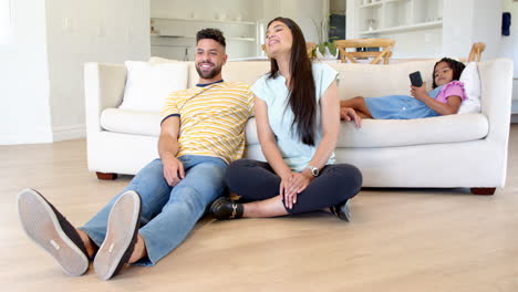 family relaxing at home, parents chatting while daughter uses smartphone on couch