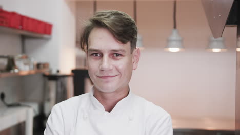 portrait of happy caucasian male chef smiling in restaurant kitchen, slow motion