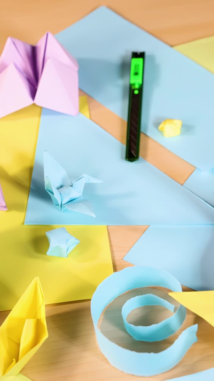 Vari animali e barche di origami disposti su carta pastello, illuminazione brillante, movimento fluido della telecamera dall'alto.