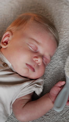lovely caucasian newborn sleeping tight holding hands up. little baby having a hairbrush in his hand. close up. vertical video