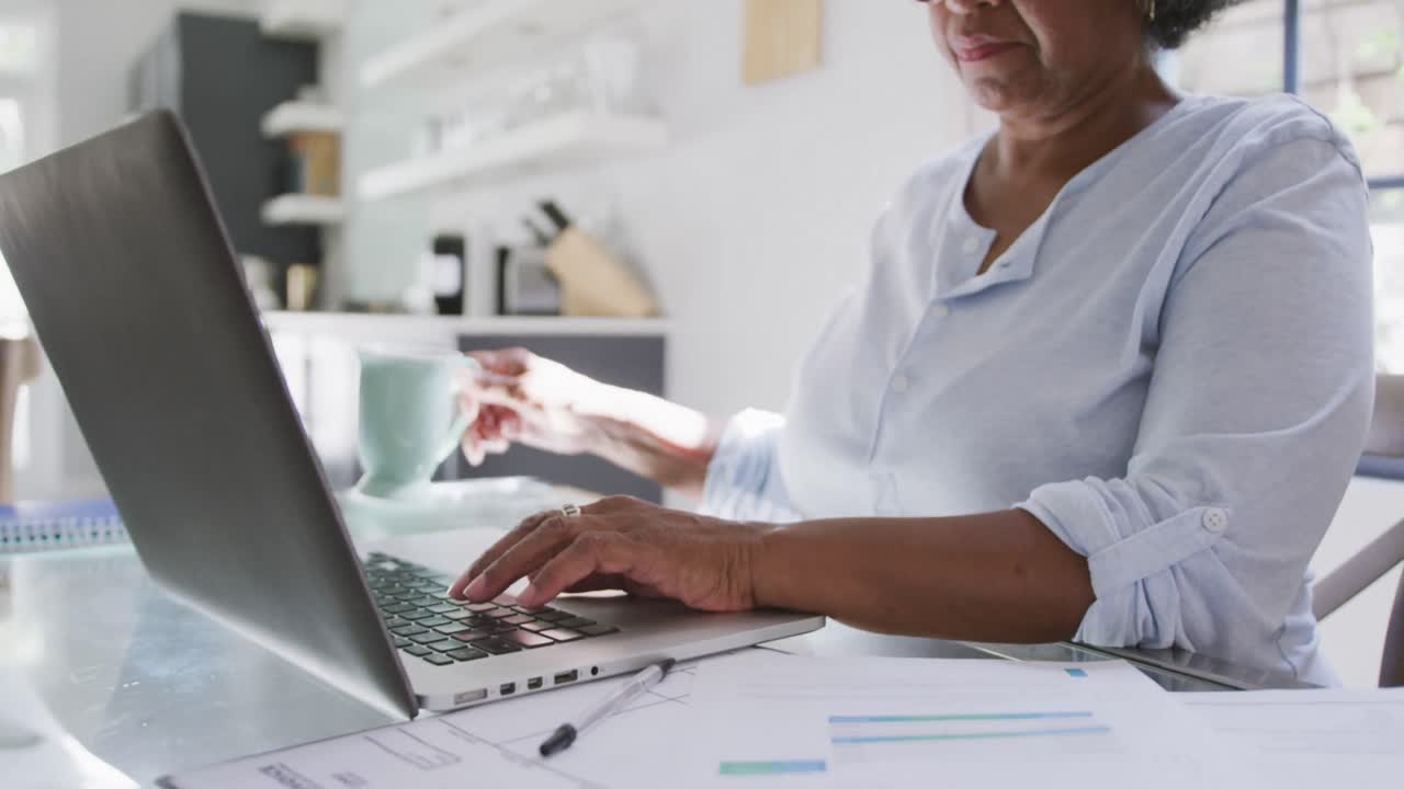 Donna anziana di etnia mista che usa un laptop. Distanziamento sociale e autoisolamento in quarantena.
