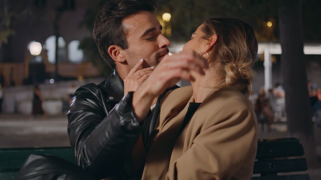 Primo piano di una coppia di fidanzati che si bacia in una strada cittadina. Un uomo premuroso accarezza la donna che lo guarda.