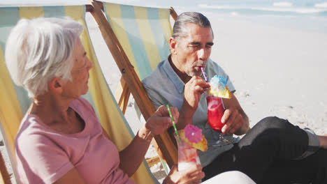 una pareja caucásica senior sentada en sillas de sol en la playa.