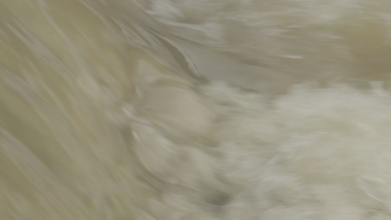 Slow motion shot, full frame of dirty brown water with lot of splashes from a small waterfall