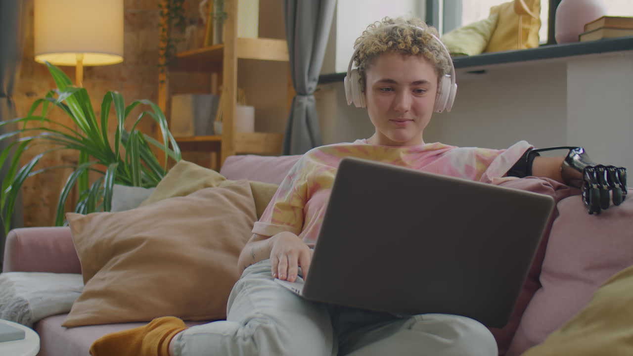 Girl with Prosthetic Arm in Headphones Video Calling on Laptop