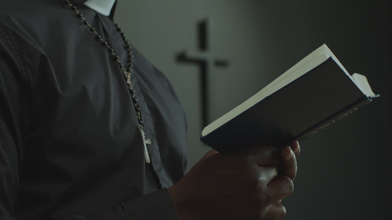 Ruce kněze v klerice držící Bibli a pronášející modlitbu během mše