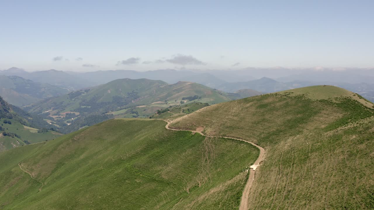 Strada sterrata accidentata che si snoda lungo un pendio montano erboso, vista aerea.