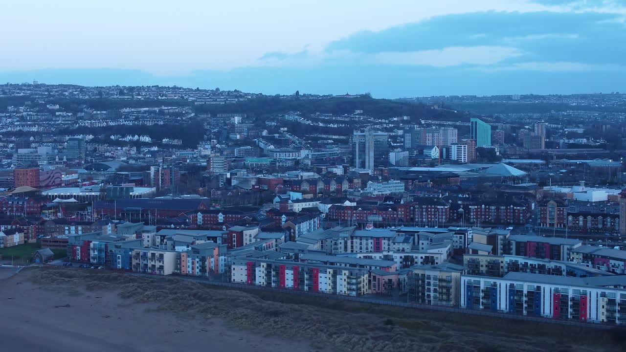 Sakte, filmatisk droneopptak over Swansea med forskjellige bygninger og boligleiligheter i tidlig blåtime-lys. Moderne by i Sør-Wales, Storbritannia.