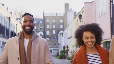 Front-view-of-multi-cultural-group-of-friends-as-they-walk-along-cobbled-mews-street-on-visit-to-city-in-autumn-or-winter---shot-in-slow-motion