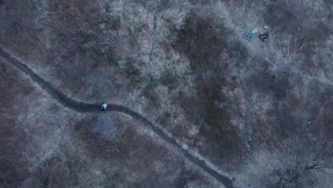 a top down view directly above two people walking on a dirt path in a park during a cloudy evening