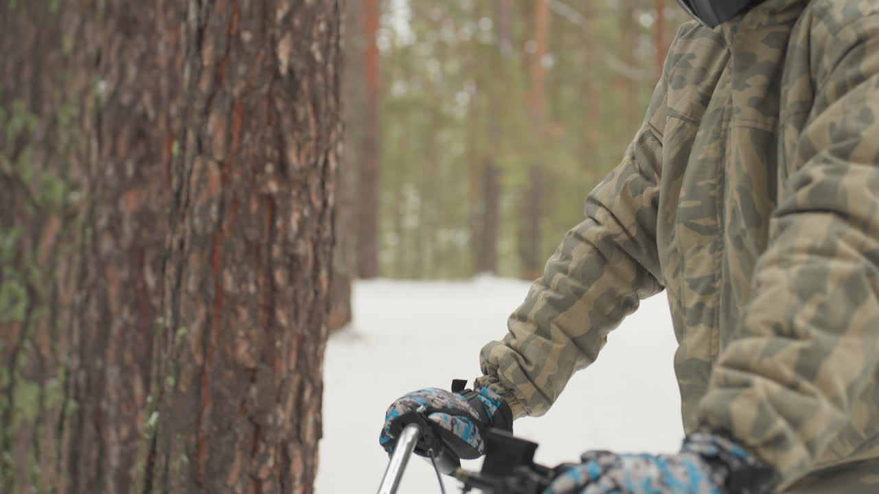 Driver gears up for challenging winter trail. Helmeted rider examines controls before intense snowy forest ride. Prepared motocross rider checks throttle and trail line amid winter pine landscape