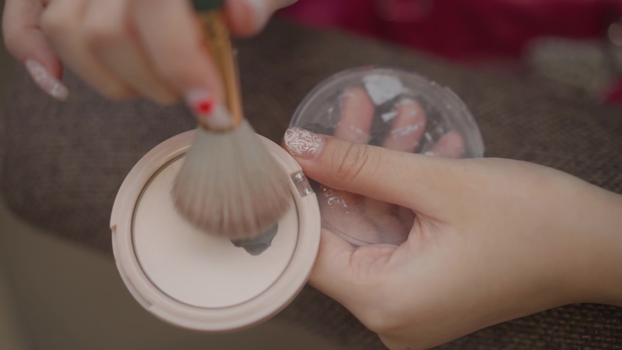 Close overhead view of hands loading dense powder brush from compact, with circular tapping and brushing motion over vanity surface, while fingers steady lid and loose powder clings to bristles