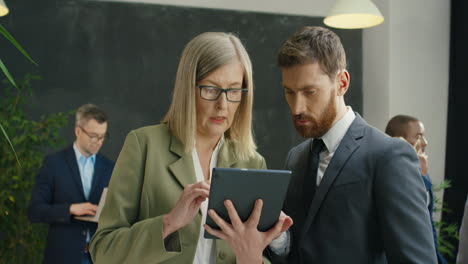 male and female business partners watching video, scrolling and tapping on a tablet at meeting in the office