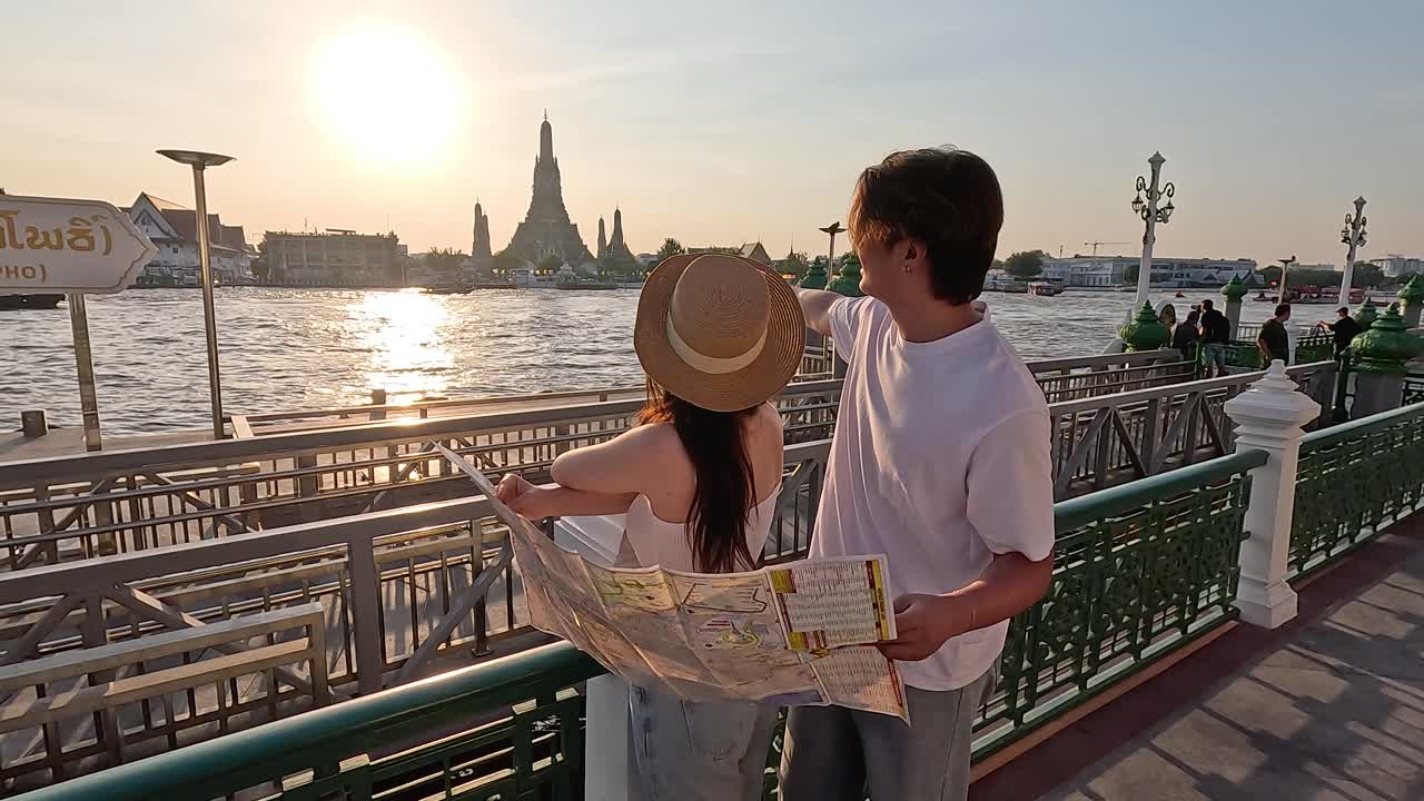 Coppia di turisti studia la mappa della città su un molo lungo il fiume al tramonto, skyline del tempio sullo sfondo