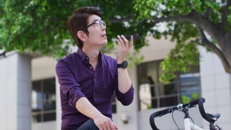 Asian-man-with-bicycle-talking-on-smartphone-while-sitting-near-the-corporate-park