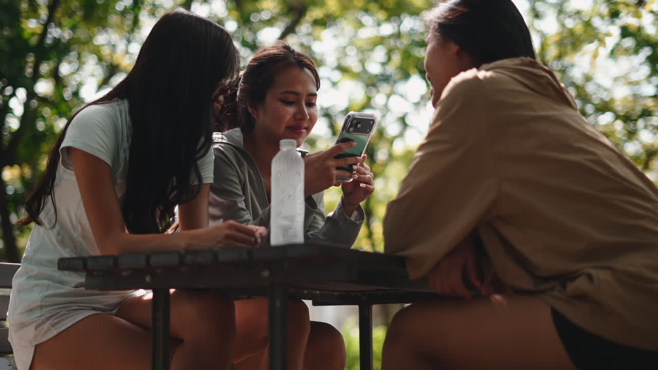 Three Young Women Friends Talking and Looking at Smartphone in Park