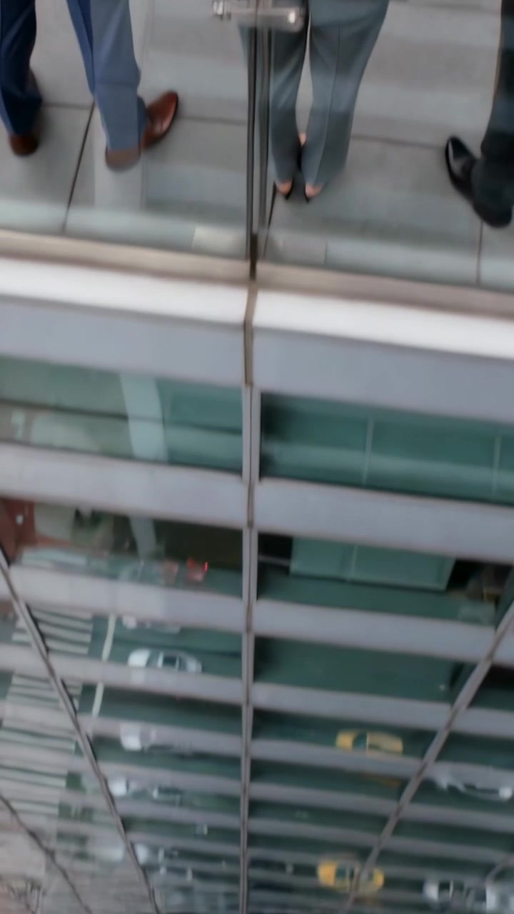 Vídeo vertical: Câmera inclinando revelando mulher em tailleur cinza em terraço com guarda-corpo de vidro, táxis.