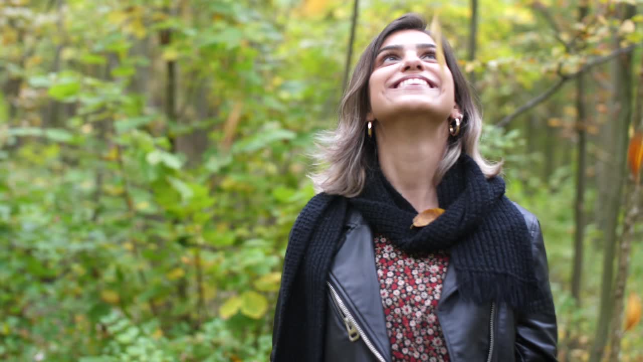 chica morena en el bosque que parece feliz en los árboles y la hoja se está cayendo