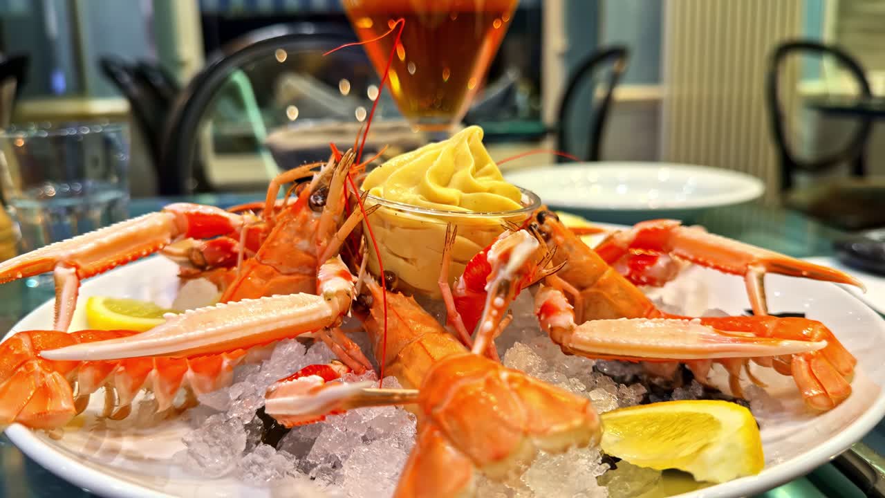 Primo piano di scampi freschi crudi su un letto di ghiaccio tritato con fette di limone e un ricciolo di burro, serviti in un ristorante con un bicchiere di birra sfocato sullo sfondo, Port-en-Bessin Normandia Francia