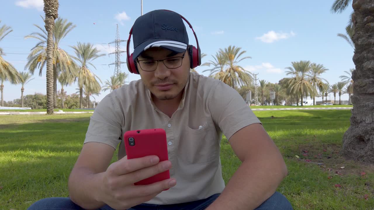 un hombre está sentado en la hierba y mirando su teléfono