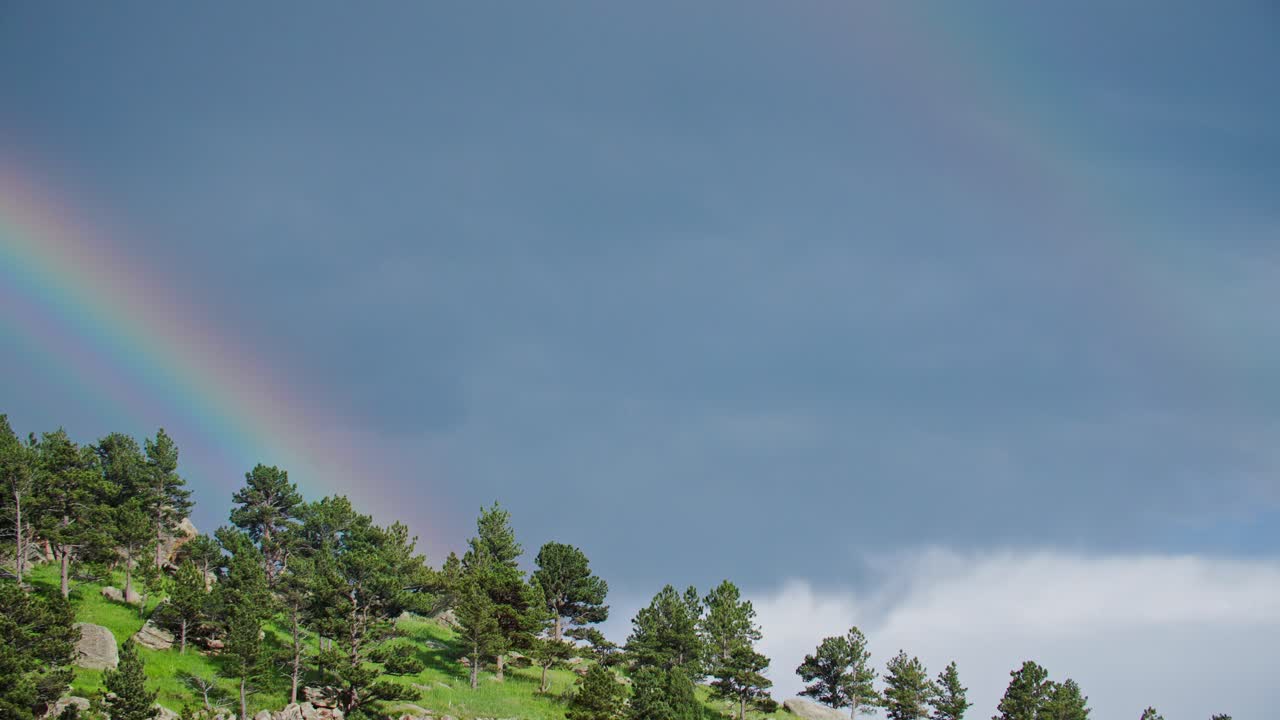 un arco iris formándose sobre los árboles en una colina en boulder, colorado, ee.uu.