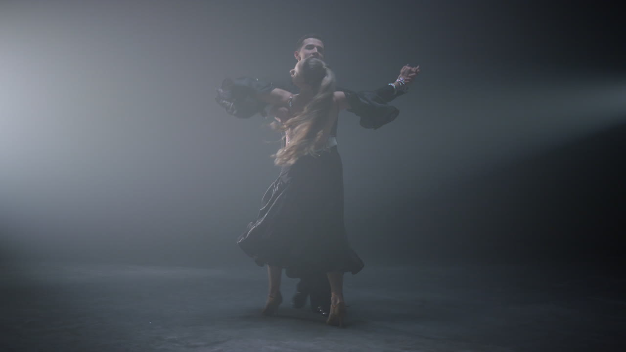 Coppia da ballo che danza un valzer su un palco buio. Ballerini sensuali che volteggiano al chiuso.