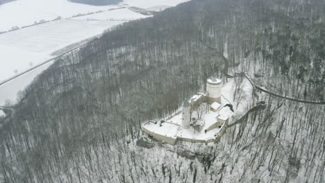 Drone-aerial-of-the-fairy-tale-castle-Plesse-in-winter-with-a-huge-amount-of-snow-on-a-beautiful-mountain-near-Bovenden,-Germany,-Europe