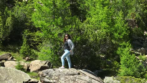 brunette woman with sunglasses poses standing on rock surrounded by nature of val masino in valtellina, italy