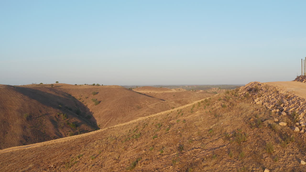 포르투갈 알가르베의 황금시간대에 흙길을 따라 앞으로 불모의 언덕과 마른 언덕 사이의 계곡을 보여줍니다.